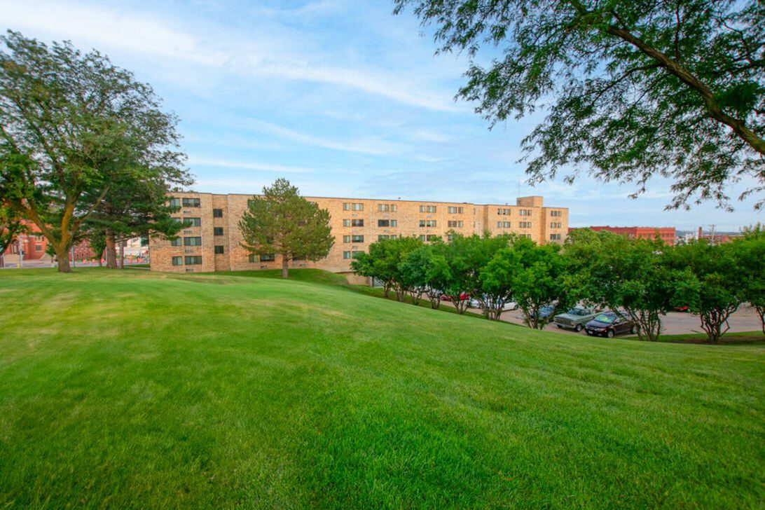 Grassy hill with brick apartment building and trees